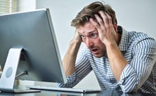 Man looks at computer monitor with his hands holding his head in apparent frustration.